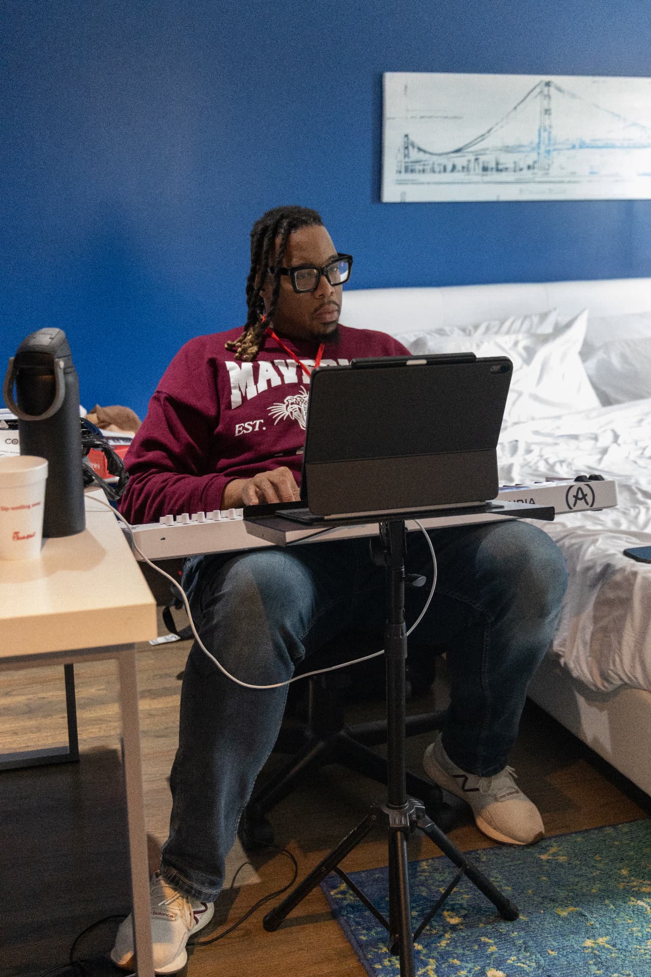 Songwriter in a maroon sweatshirt playing keys with a laptop in front of him