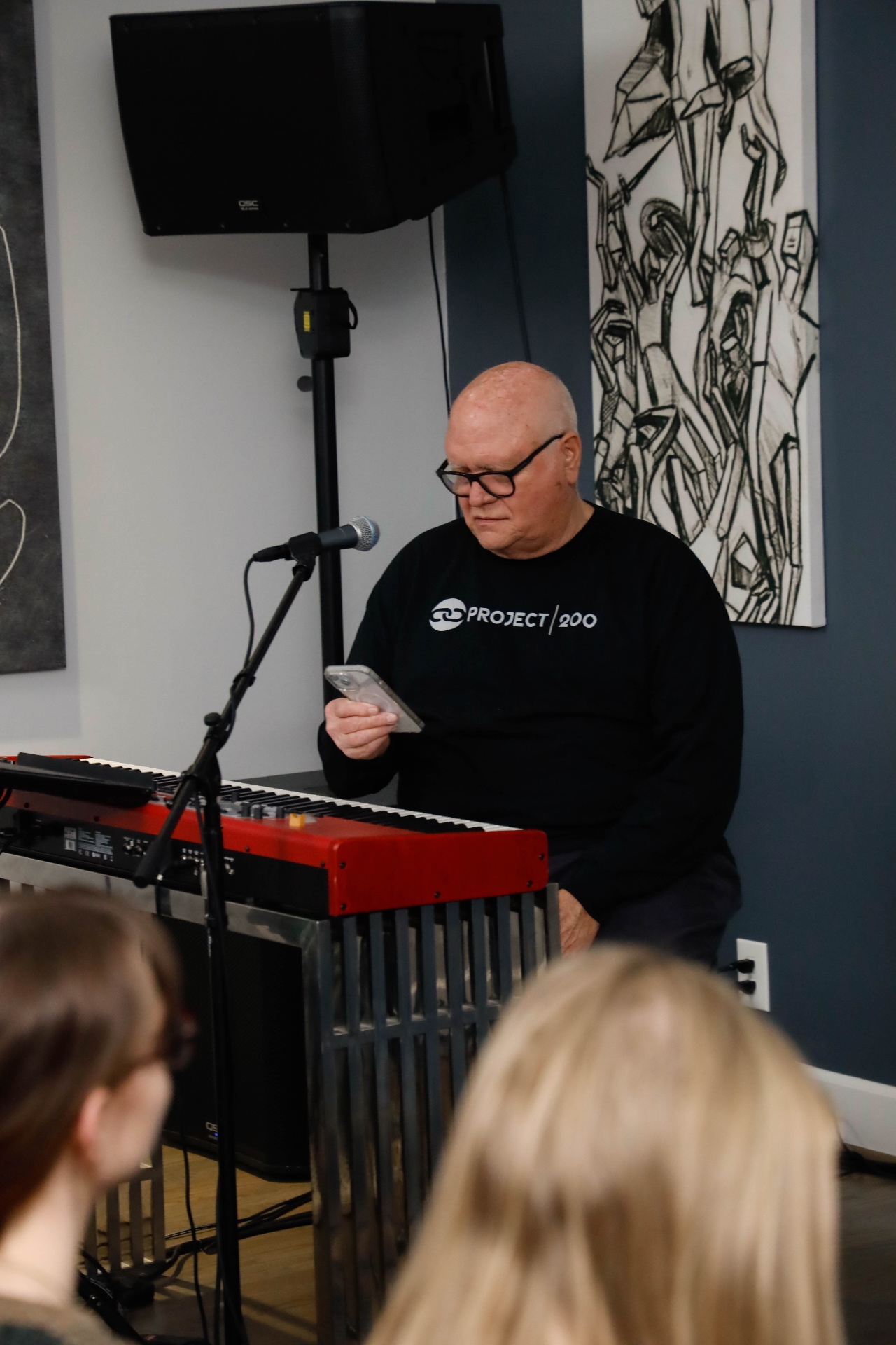 Keyboard player seated behind a red piano reading from a phone