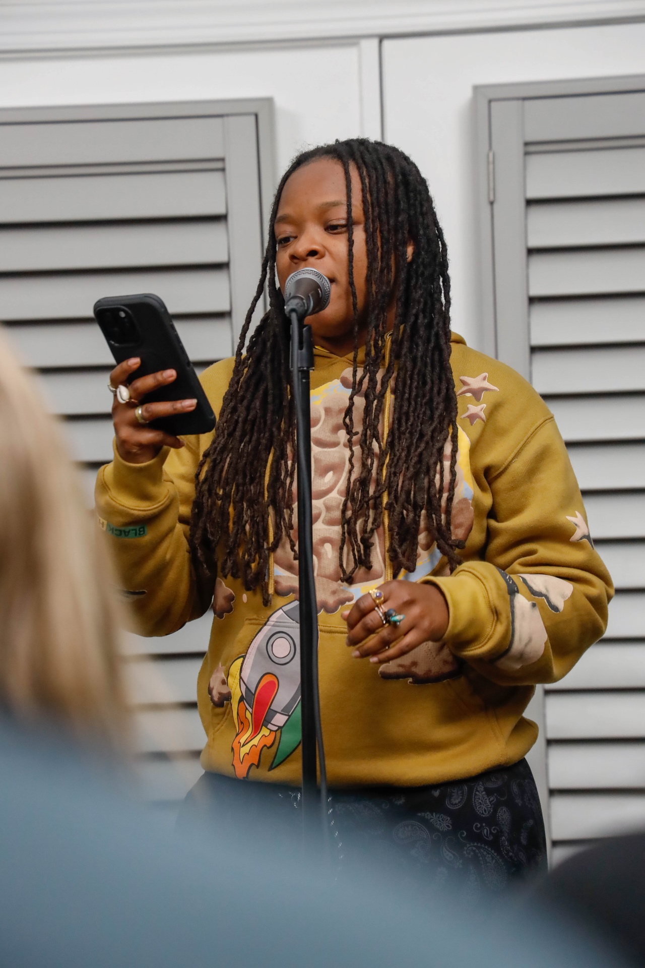 Performer in an olive hoodie reading lyrics into a microphone
