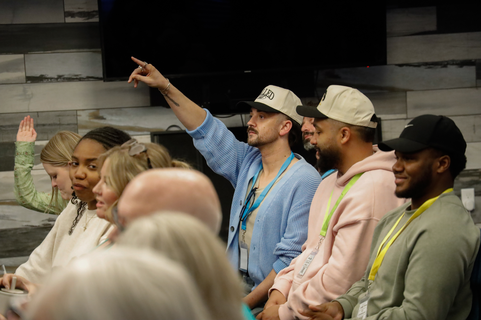 Attendee in a blue cardigan and 'Called' cap pointing toward the front of the room