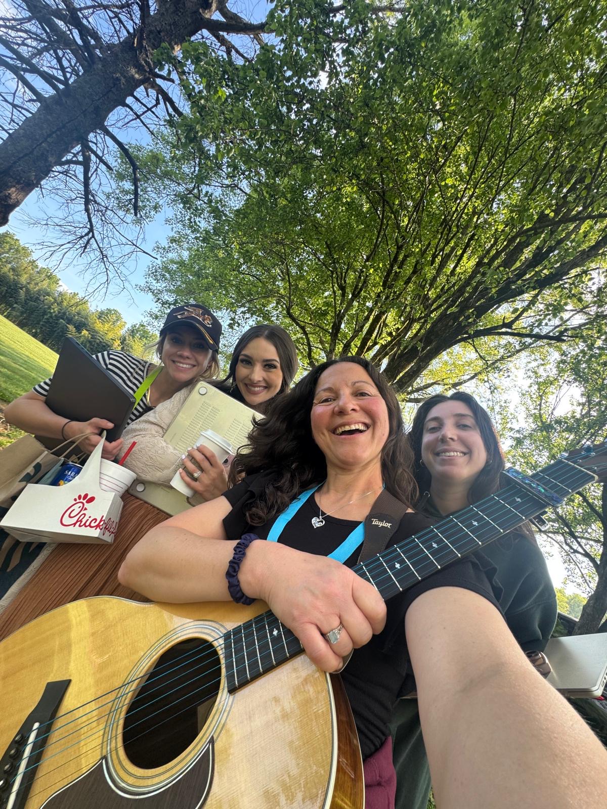 Songwriters laughing outside with a guitar and coffee