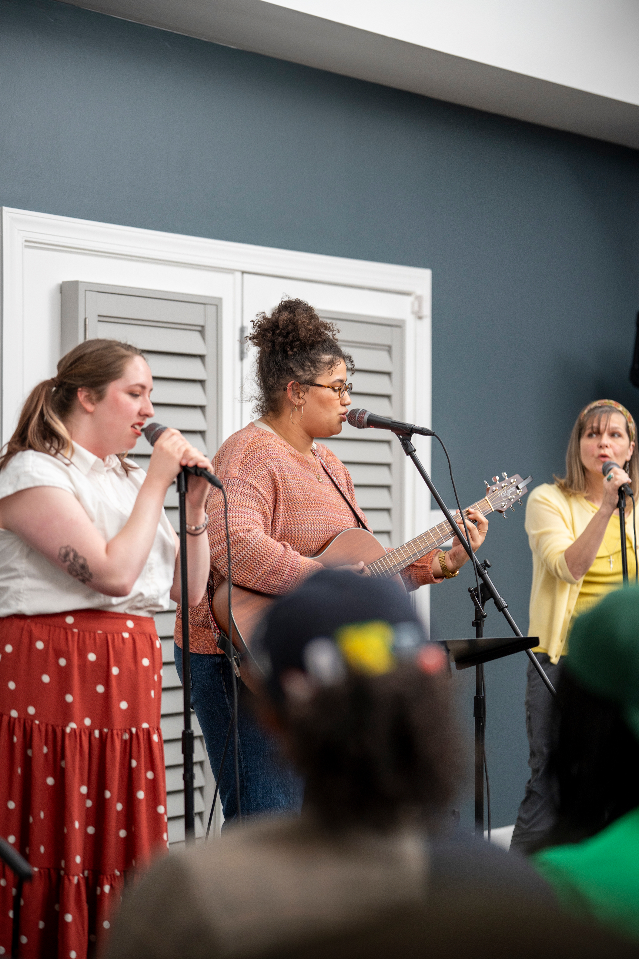 Three performers singing together with acoustic guitar and microphones
