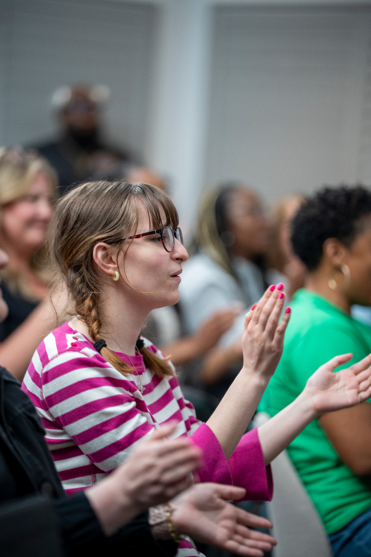 Audience member in a pink striped shirt clapping during a session