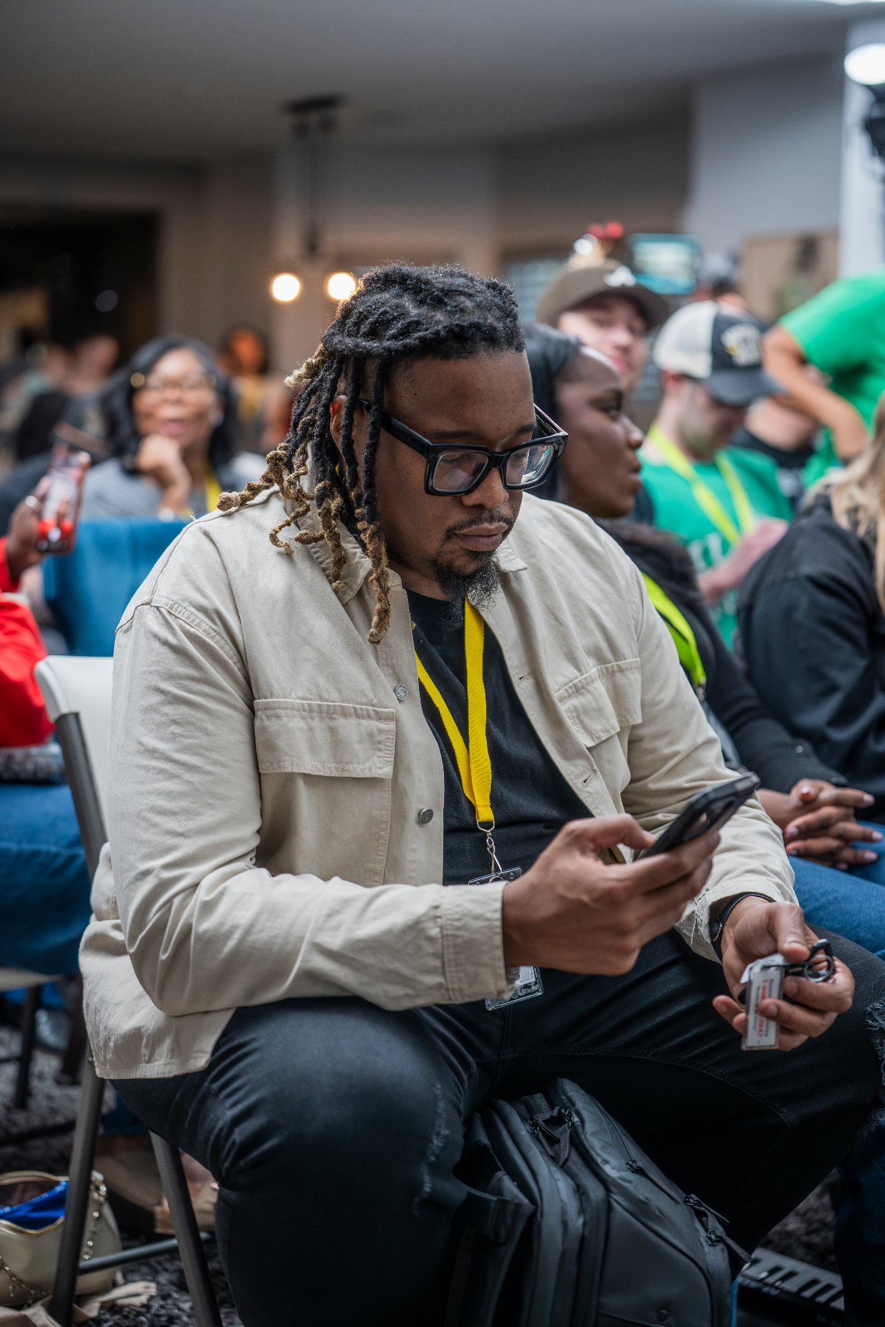 Audience member seated with a yellow lanyard checking a phone between sessions