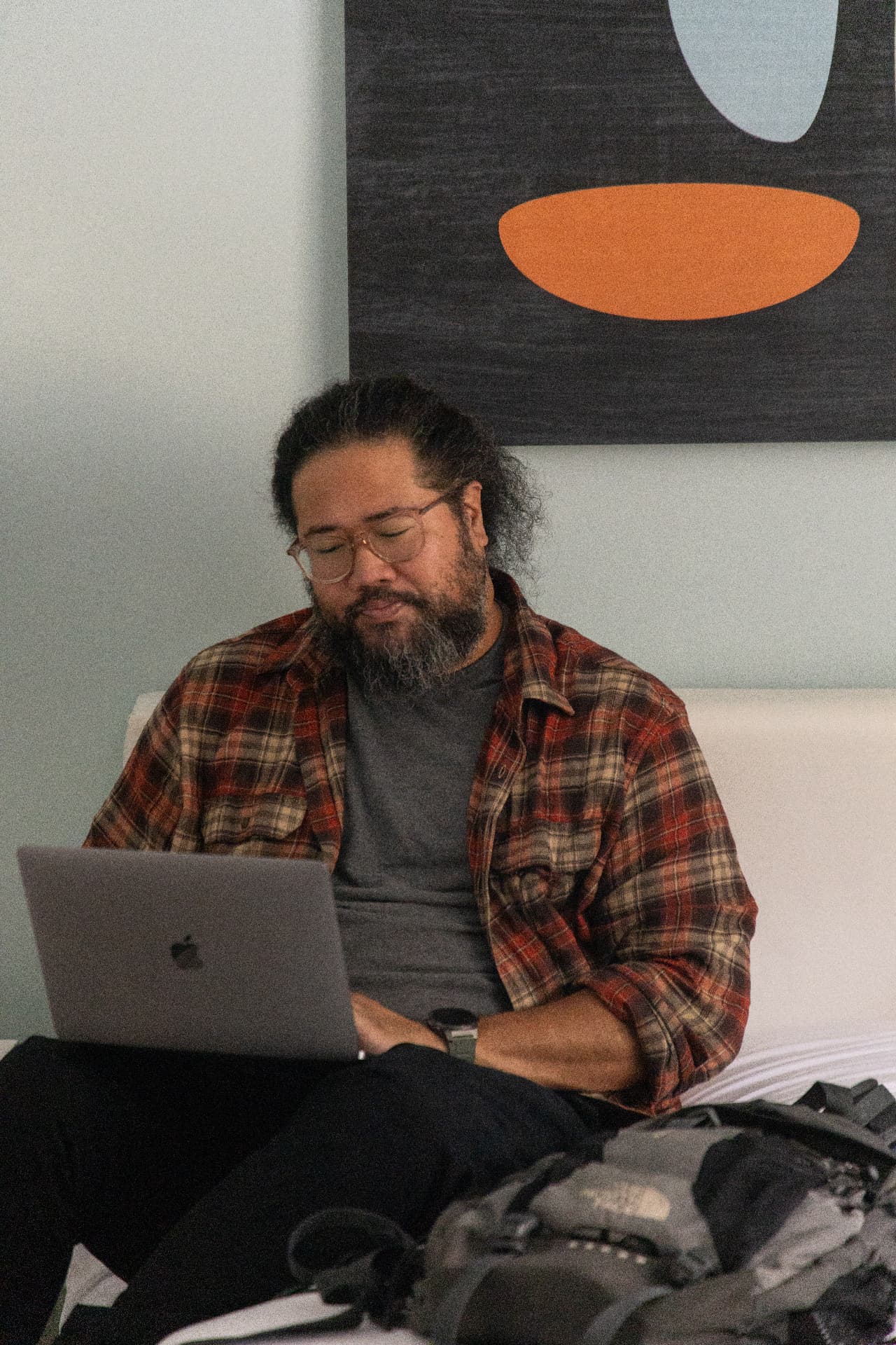 Bearded songwriter writing on a laptop in front of a painting
