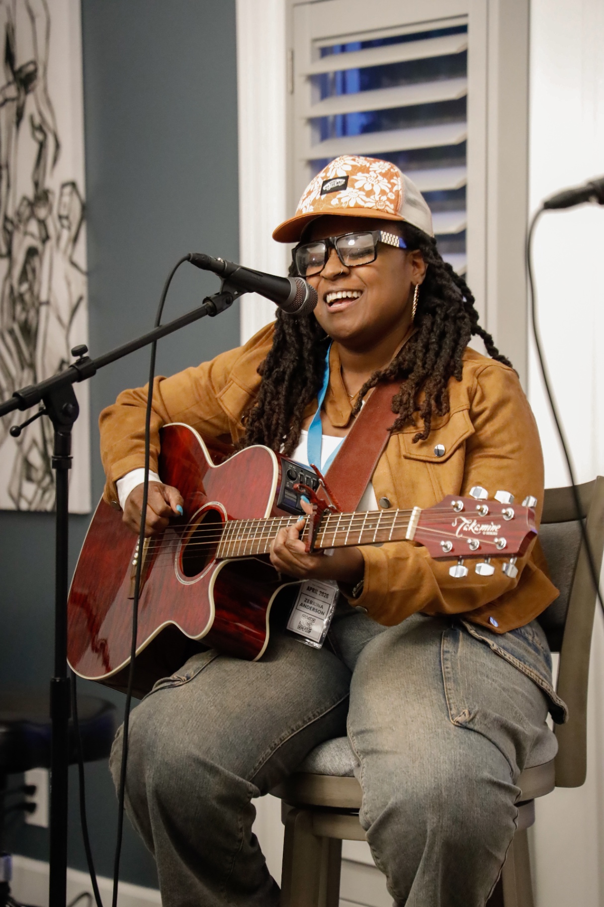 Songwriter in an orange floral cap smiling while playing a red acoustic guitar