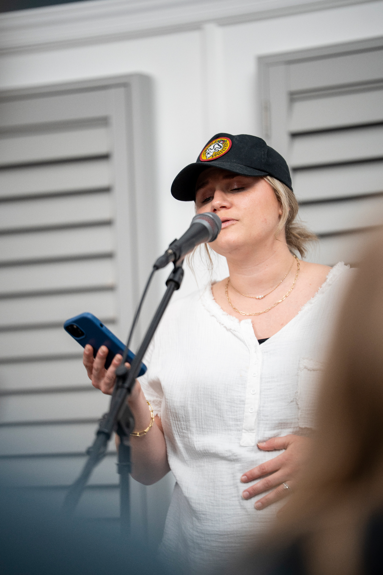 Performer in a white top singing with eyes closed while holding a blue phone