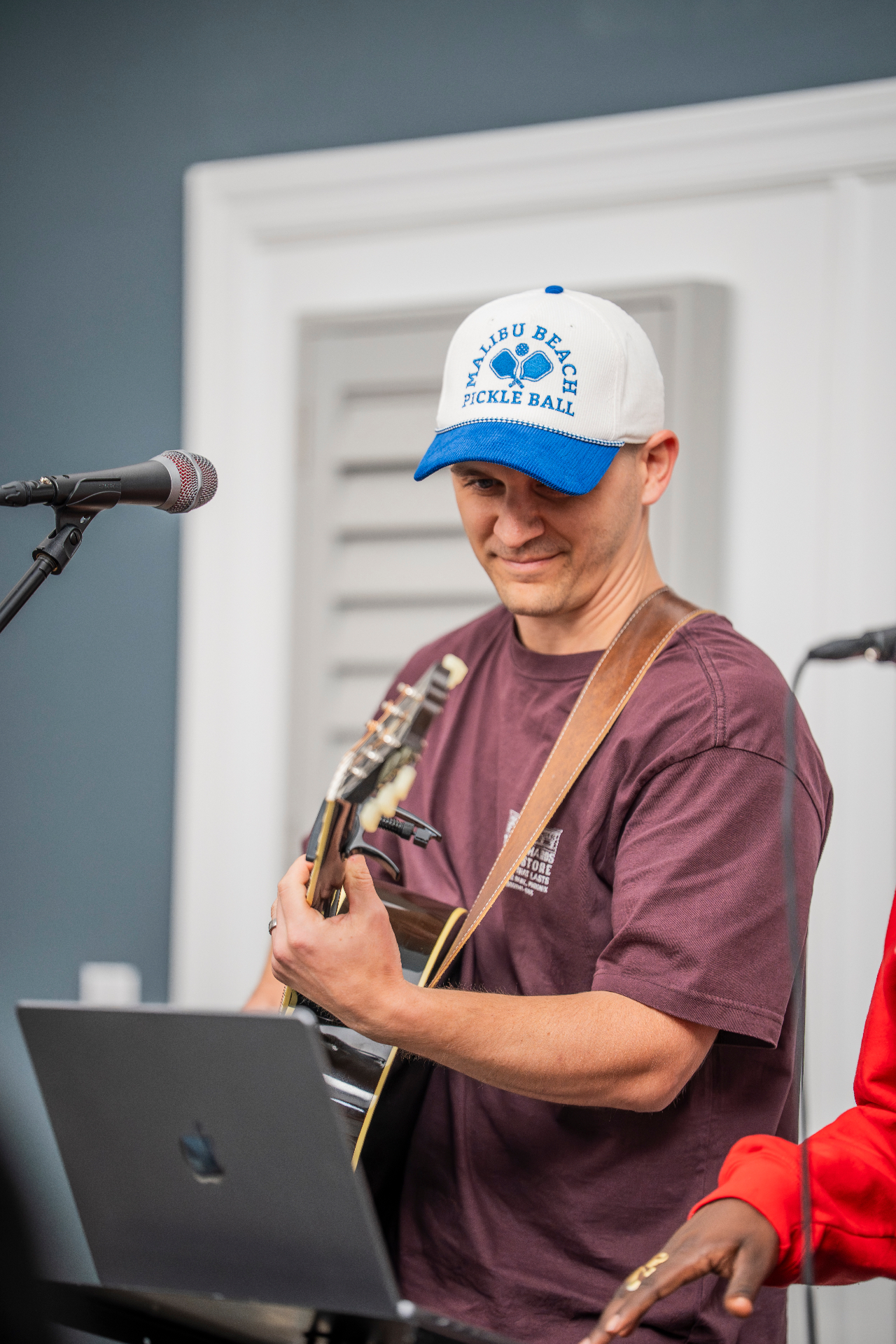 Guitarist in a white and blue cap smiling during a live performance