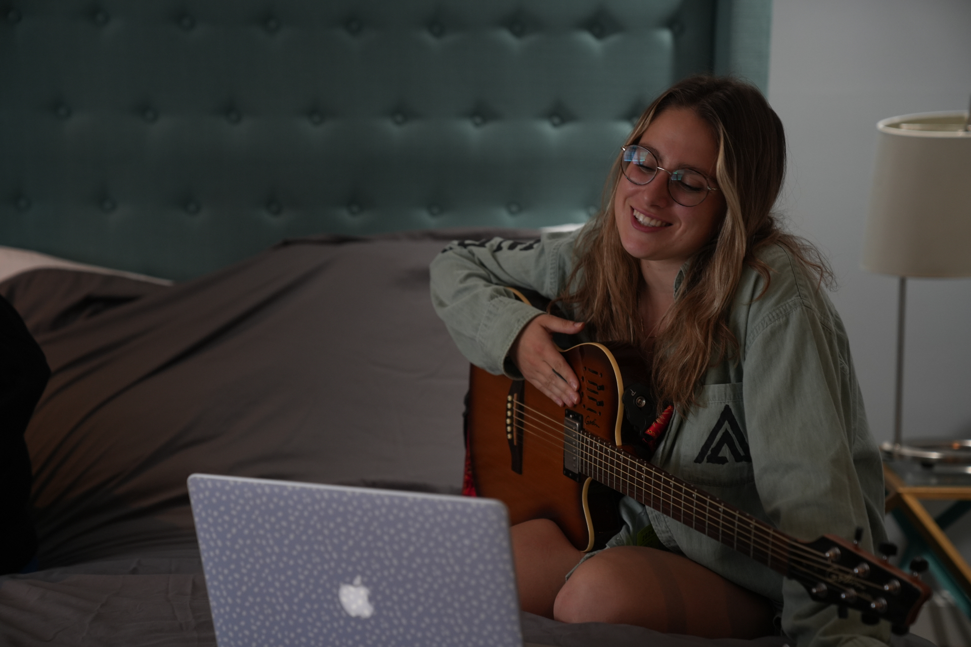Songwriter smiling while playing guitar with a laptop nearby
