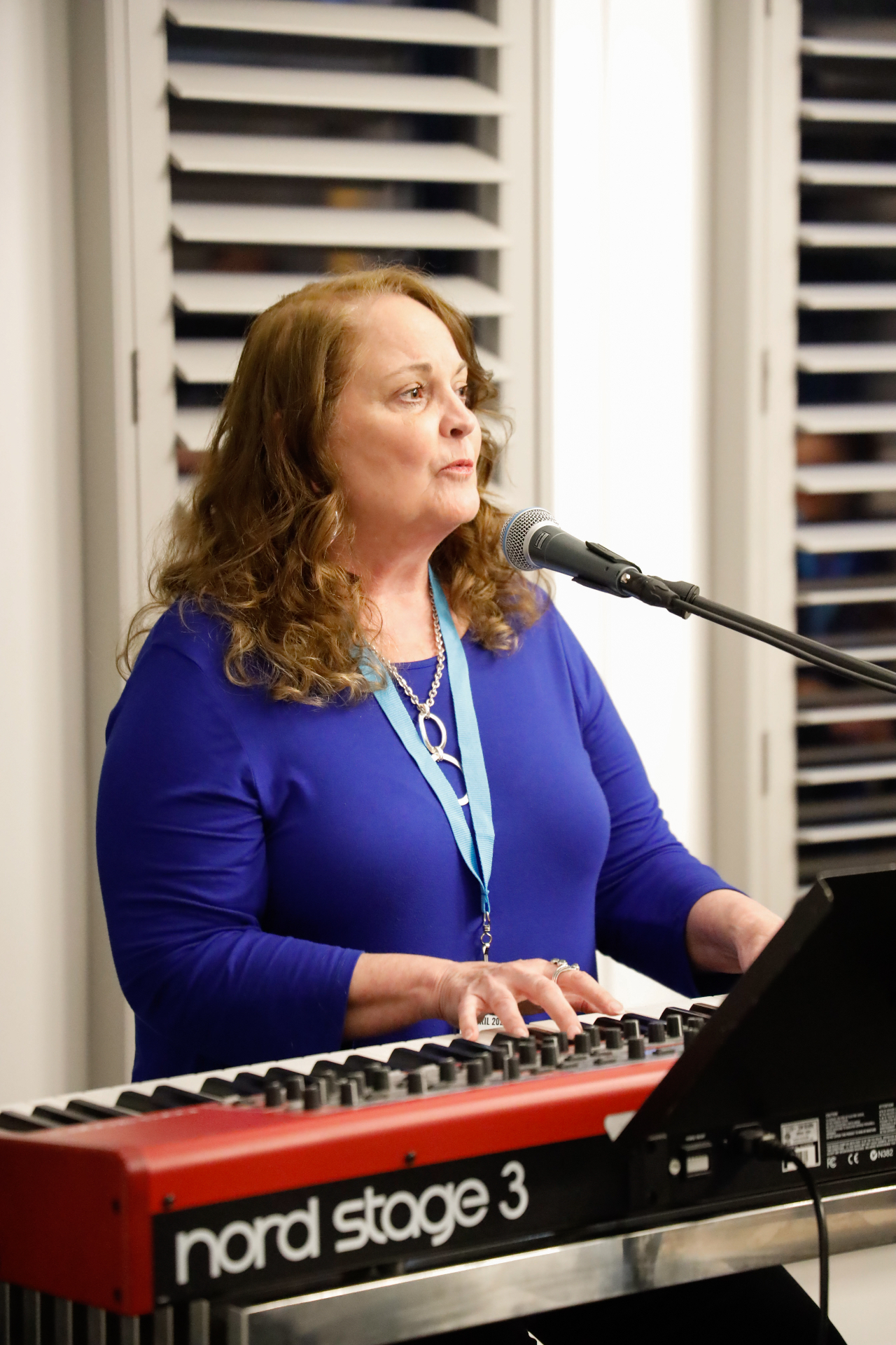 Vocalist in a blue top singing while playing a Nord Stage 3 keyboard